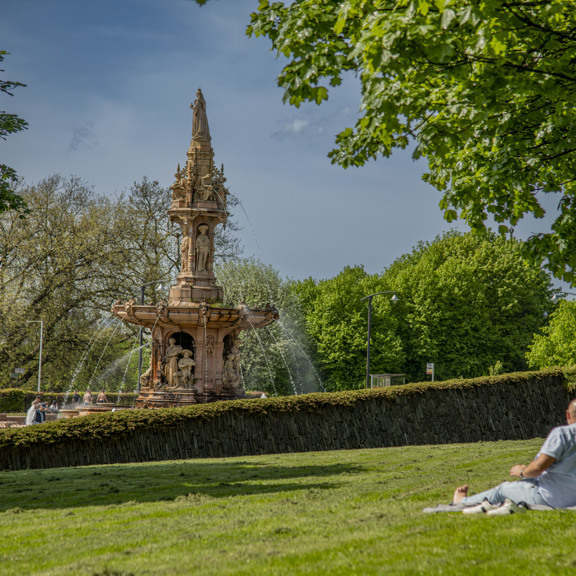A couple lazing in the sunshine near the large terracotta, five-tier, French Renaissance-style Doulton Fountain in Glasgow Green