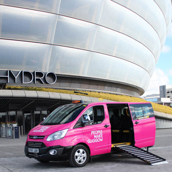 pink taxi with People Make Glasgow branding in front of a modern concert arena, with the ramp down
