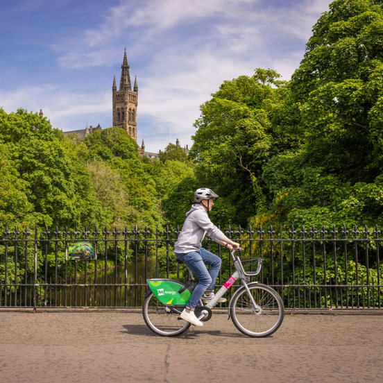 Cyclist, with tower of the Gothic revivals style spire of the University of Glasgow in the background, surrounded by greenery