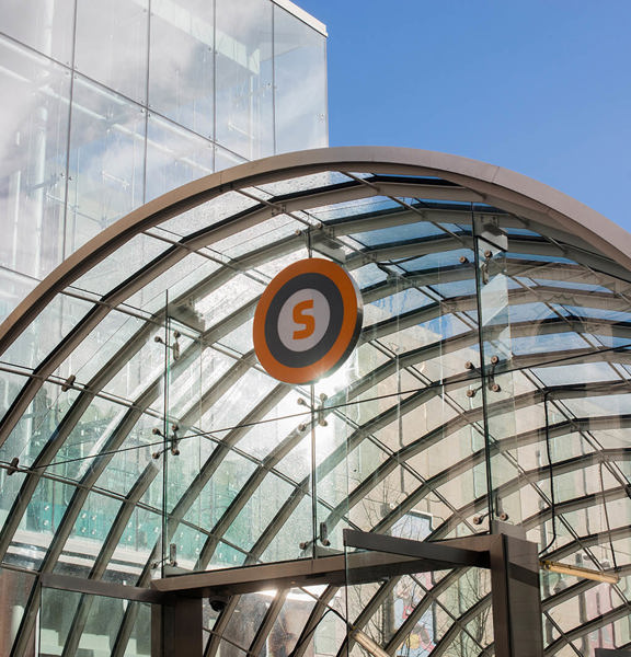 modern glass dome Subway entrance with an orange, grey and white circular sign with a large letter S in the middle