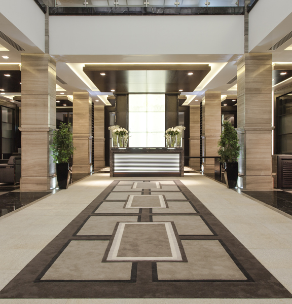 200 Conference & Events Ltd Grand Hall. A large, symmetrical entrance area decorated in muted tones, there are potted plants and vases of cut flowers decorating the reception desk