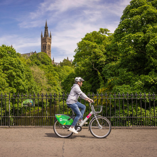 Cyclist, with tower of the Gothic revivals style spire of the University of Glasgow in the background, surrounded by greenery