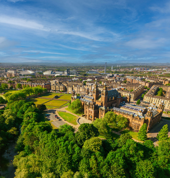 Glasgow cityscape, with the Baroque-style Kelvingrove Art Gallery and Museum, surrounded by greenery. The modern buildings of the Scottish Event Campus and the Glasgow Science Centre are visible in the background