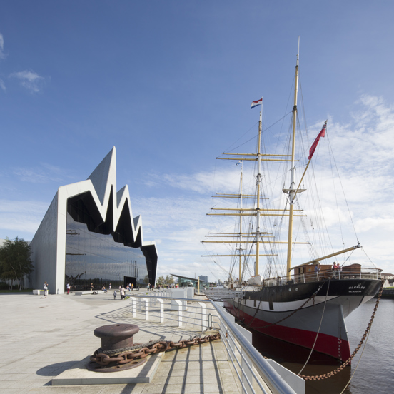 Sunny view of the modern, glass-fronted Riverside Museum, where the roofline reminiscent of a heartbeat on a monitor, with a three-masted 19th century Glenlee tallship docked outside.