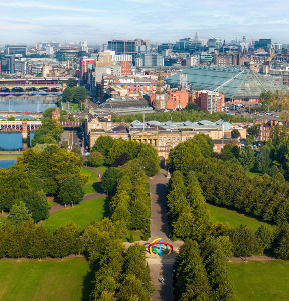 Sunny view of the tree-lined paths of Glasgow Green, on the bank of the River Clyde with several bridges and Glasgow city centre in the background