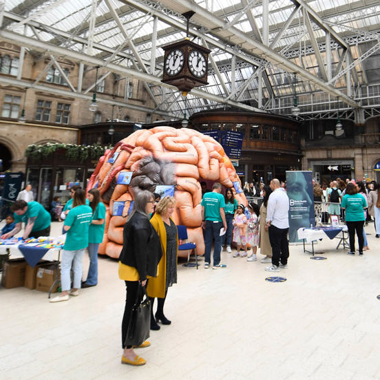 people milling around a large inflatable brain in a train station