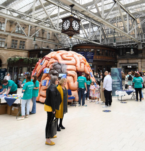 people milling around a large inflatable brain in a train station