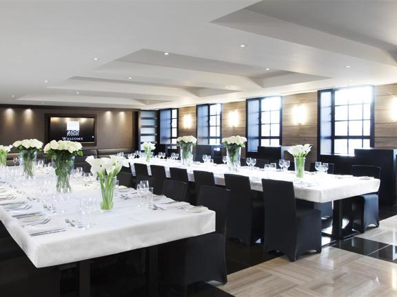 The Restaurant at 200 Conference & Events Ltd, two long tables are covered with white tablecloths, there are vases of cut flowers and wineglasses laid out on the tables.