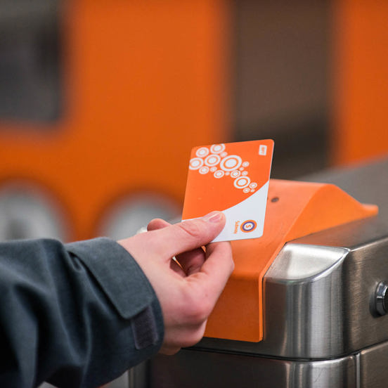 hand holding an orange and white travel card reading Subway to a scanner
