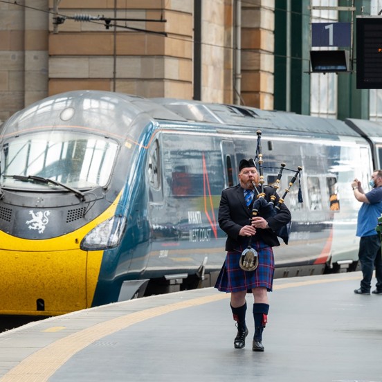 Train arrives at station with bagpiper playing on the platform and visitors arriving